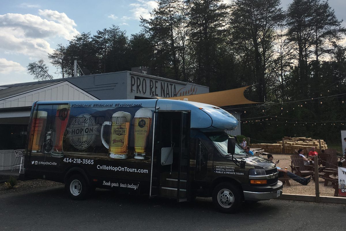 A wrapped Hop On shuttle in front of Pro Re Nata brewery at dusk, string lights over the patio crowd