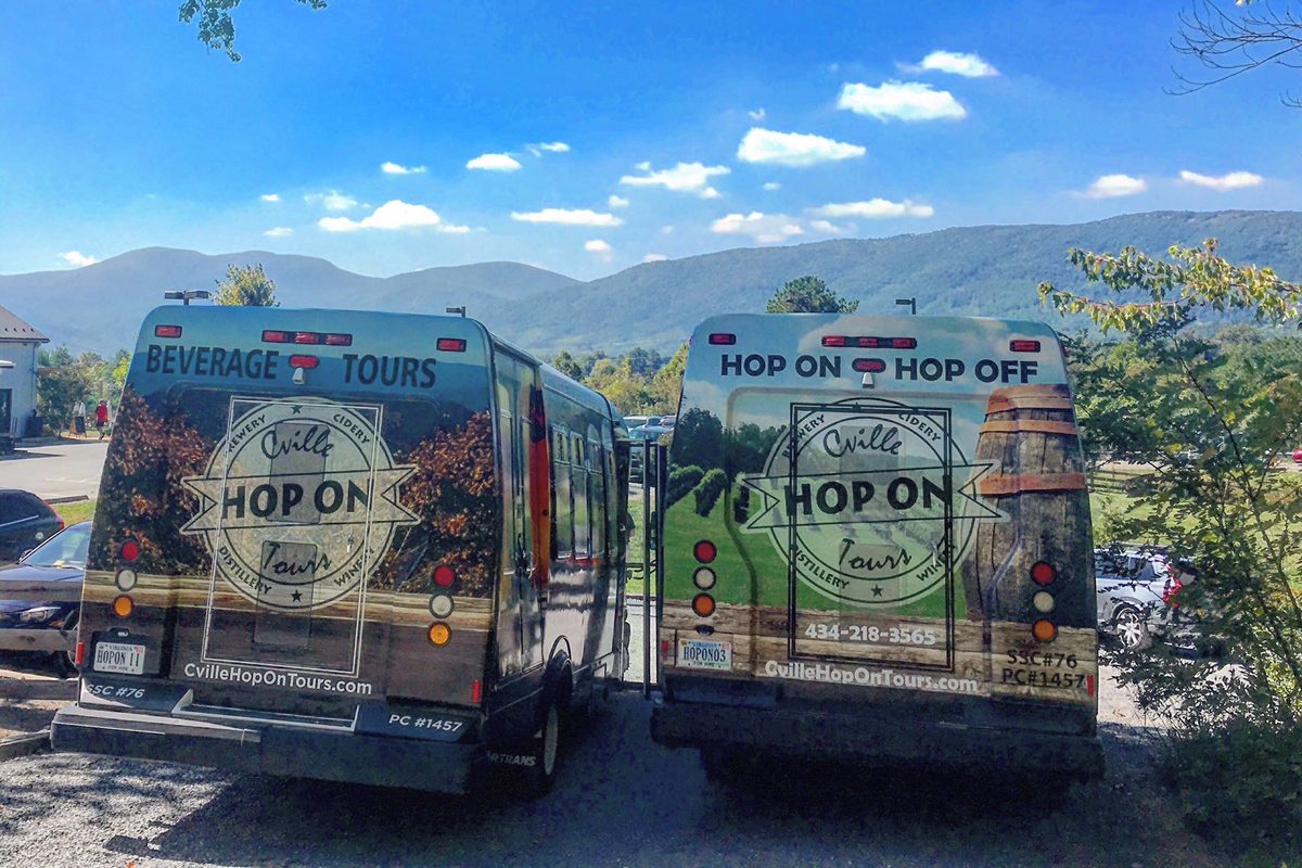 The backs of two Hop On shuttles side by side, one reading Beverage Tours and the other Hop On Hop Off over the roundel, mountains behind