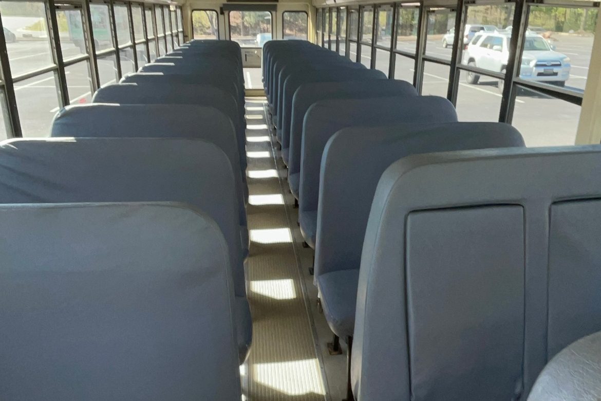 Inside the grey school bus: grey bench seats on both sides of a center aisle