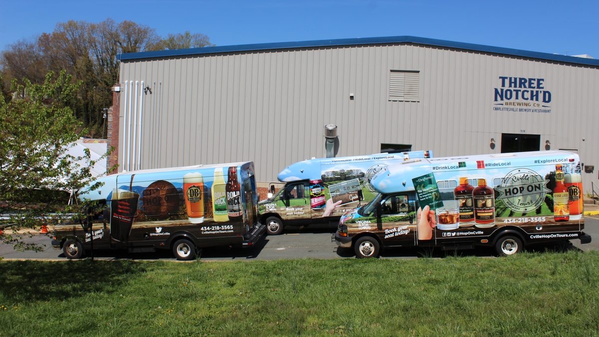 Three wrapped Hop On shuttles parked on the grass in front of the Three Notch'd Brewing building